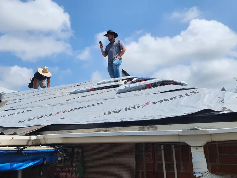 Two roofers on a roof wrapped in synthetic underlayment during a full roof replacement